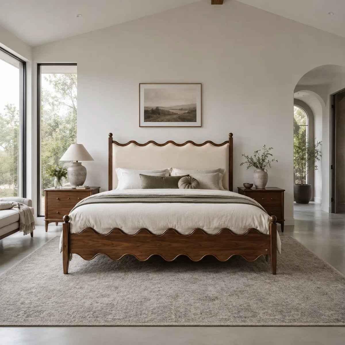 A scalloped wooden bed frame with a cream upholstered headboard is centered in a bright, modern bedroom with matching wood nightstands, a gray rug, and large windows.