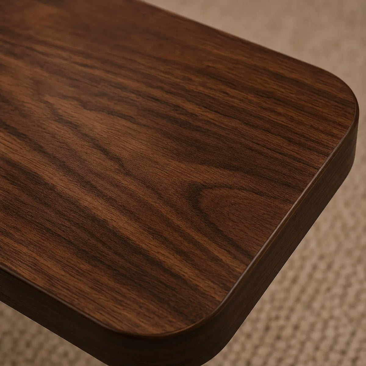 Close-up of a dark brown wooden table corner with rounded edges and visible wood grain, set on a beige woven rug.