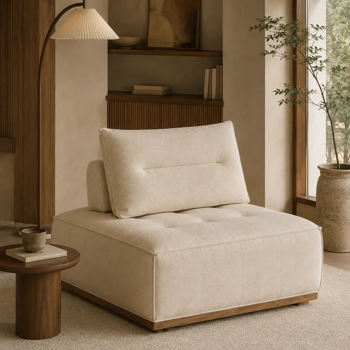 A cream-colored tufted lounge chair with a matching back cushion, styled in a warm, modern minimalist room with a wooden floor lamp, a small wooden side table, and a potted plant.